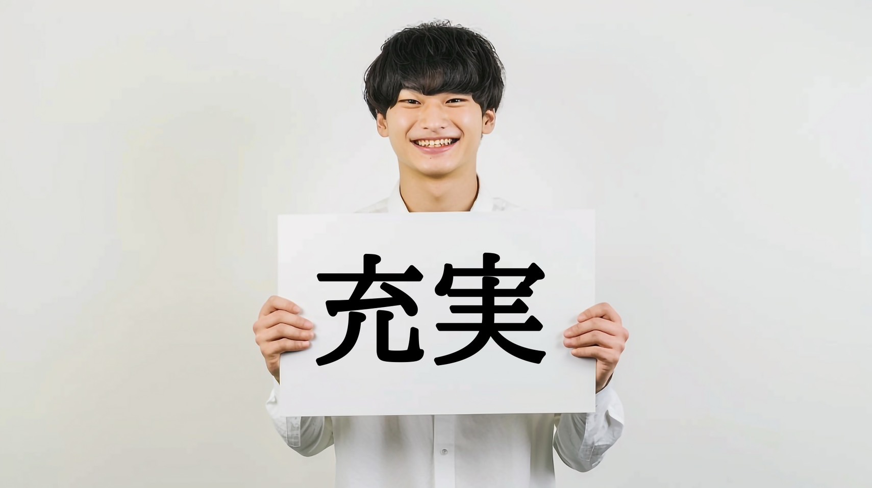 充実と書かれたプラカードを掲げた男性